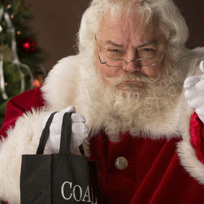 pictures of Real Santa Claus has his bag of coal for the naughty. This stock image is a horizontal composition with a christmas tree and brown background.